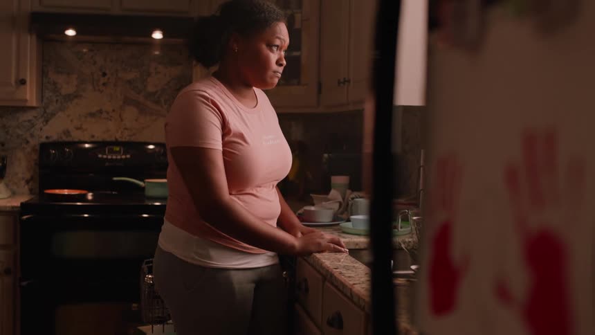 Dirstressed black woman standing at kitchen sink looking out the window