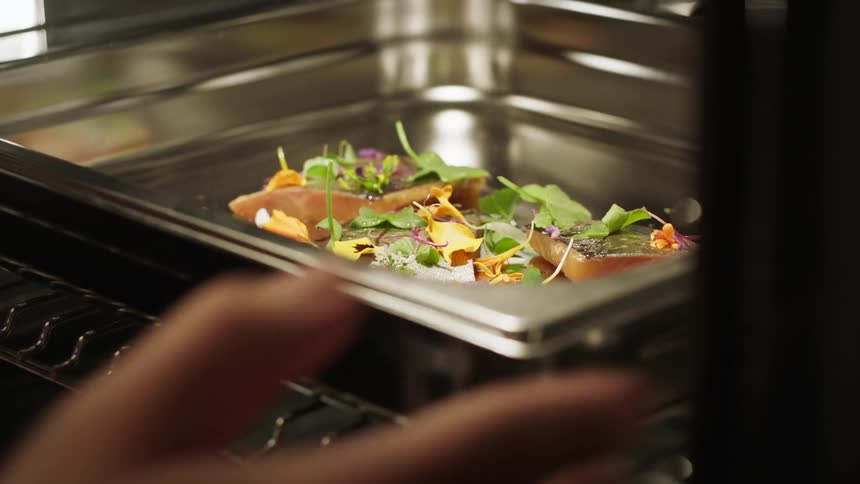 A womans hands placing a salad into an oven