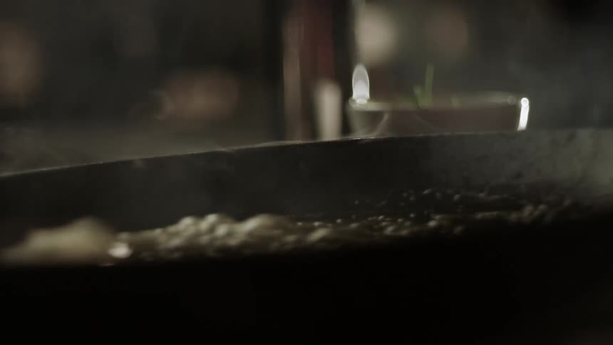 Steam rises from a pan with food sizzling on a stove