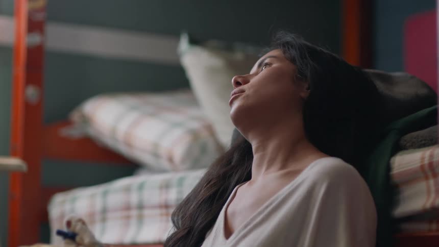 A woman sighs and lets her head fall back against a bed