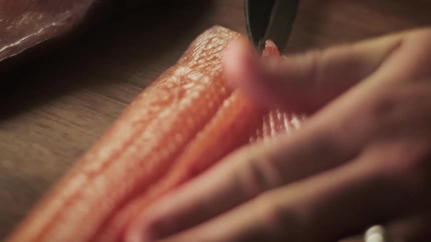 Hands of a person with a knife carefully cutting a piece of salmon