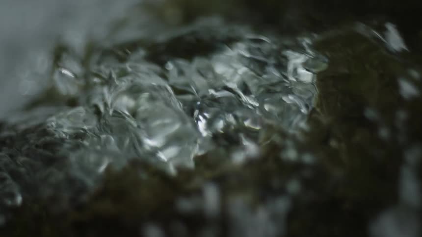 Closeup of the running water of a river on top of a rock in slow motion