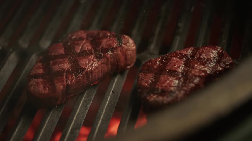 Two pieces of meat are being grilled on a grill with fire lights