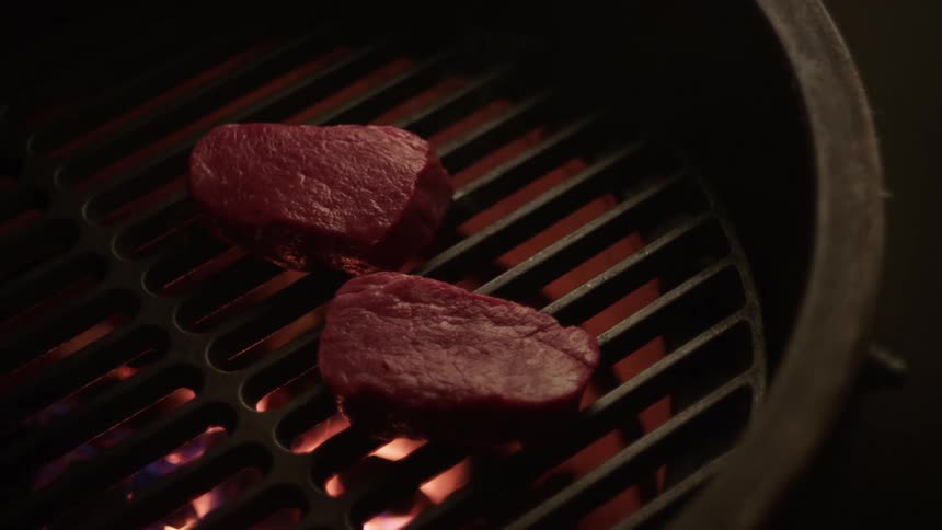 Hand of a person with a spatula placing a piece of meat on a barbecue grill