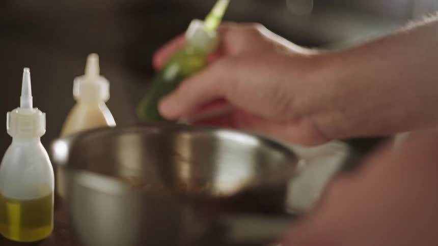 Closeup of a persons hands pouring a sauce into a small pan and stirring with a spoon