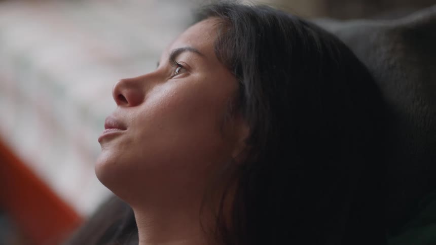 A woman sighs and leans her head against a bed
