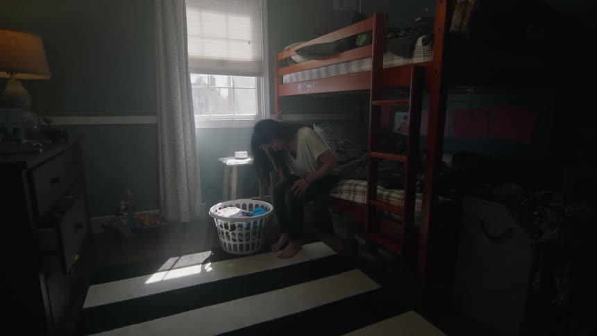A woman sitting in a bunk bed crying over a laundry basket