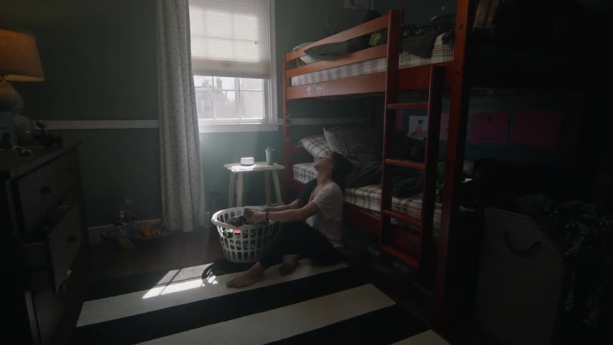 Woman leans against bed while sitting on thefloor with a basket of laundry
