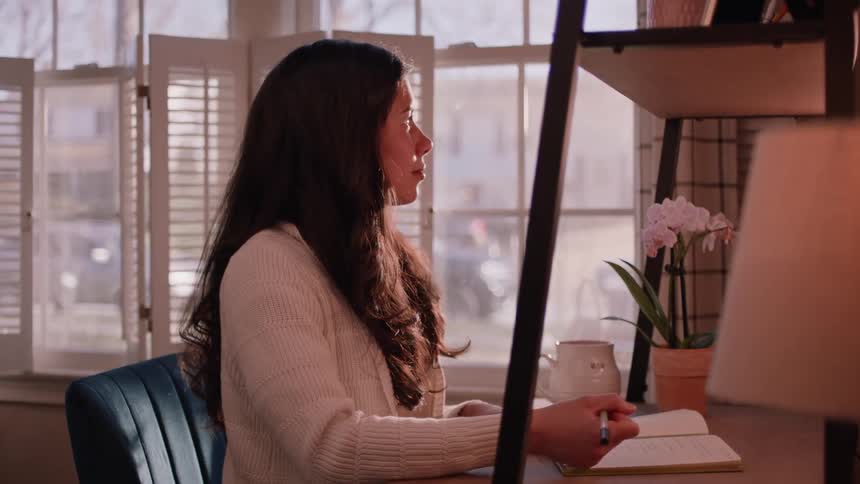 Smiling woman sitting at an office desk writing in a notebook with a pen