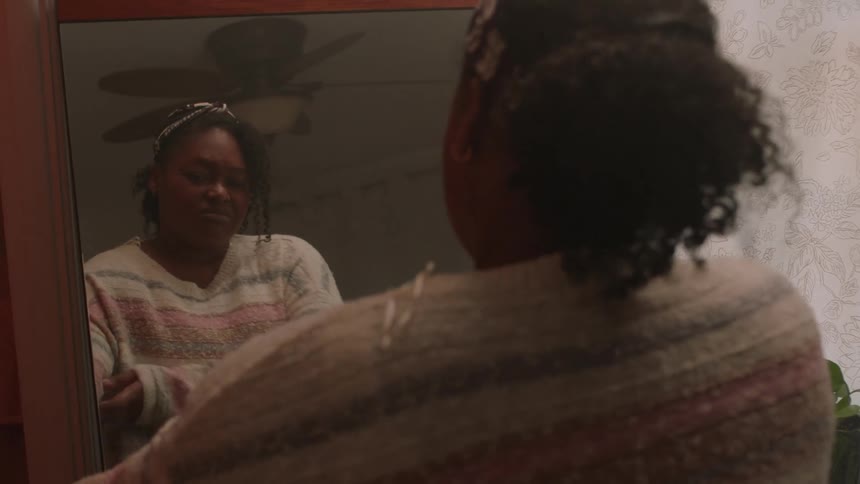 A woman is looking in the mirror and she takes off her blue shirt and then puts on a white sweater