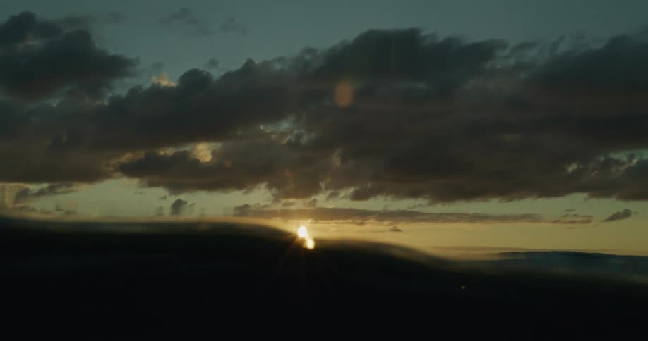 Sun shines from red tinted horizon across ocean on a cloudy day