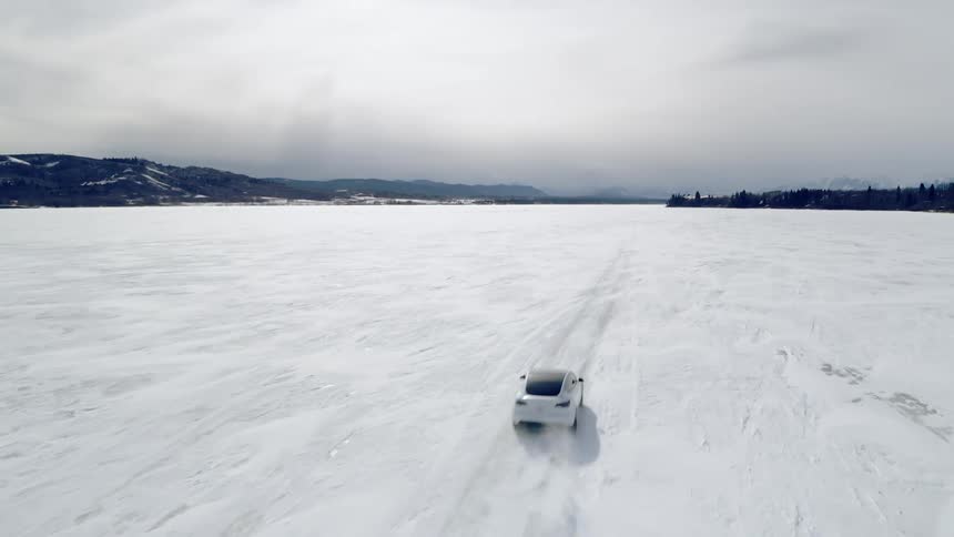 White sports car traveling at high speed on a frozen lake with mountains and forests around