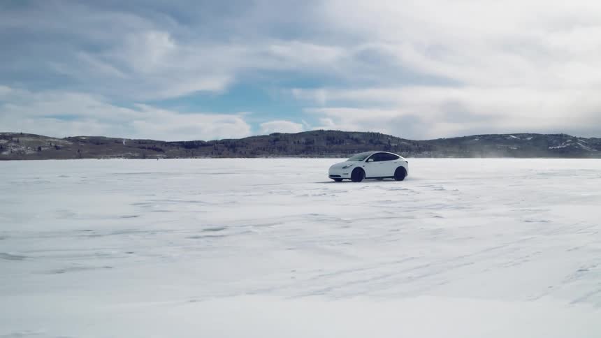 A white electric car drives across a frozen lake on a cloudy winter day