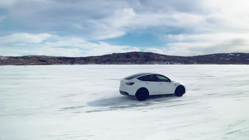 White sports vehicle traveling on snowcovered ground with mountains on the horizon