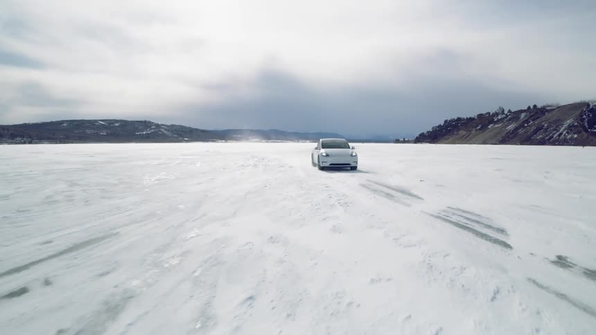 Vehicle drives on a frozen lake between mountains and hills