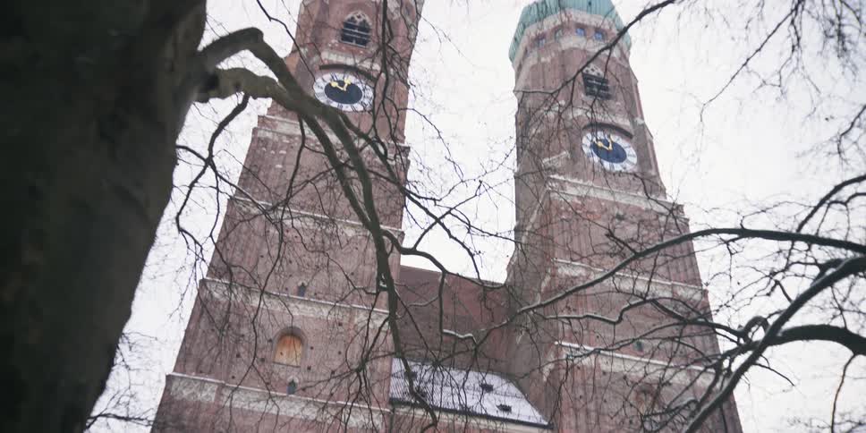 Cathedral with two clock towers stands over leafless trees under an overcast sky
