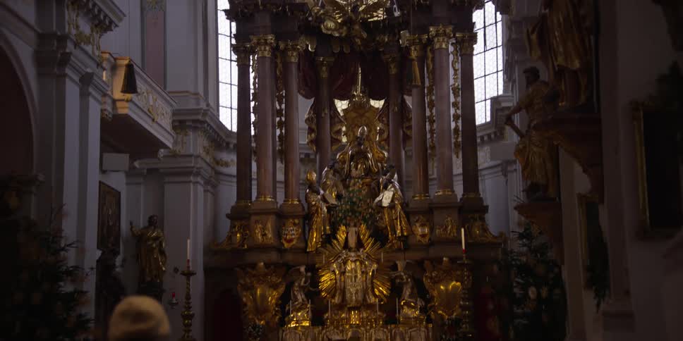 Two parishioners sit in pews viewing a very ornate altar in a cathedral
