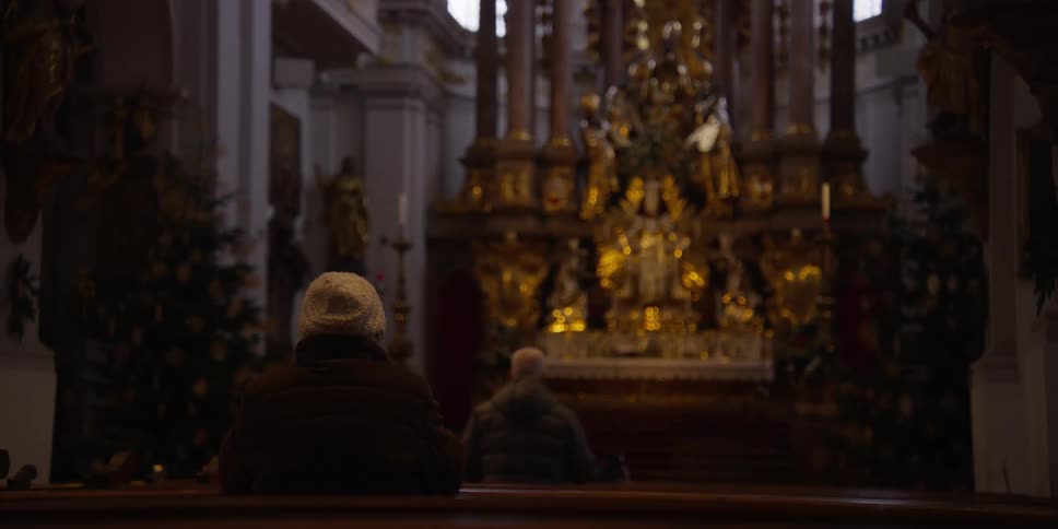 Two people praying inside a large church with an ornate golden altar