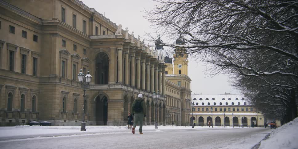 People walking on a snowy street next to a museum on a cloudy day