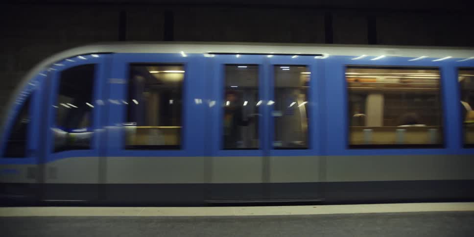 A blue subway with several windows arriving at a station with concrete walls