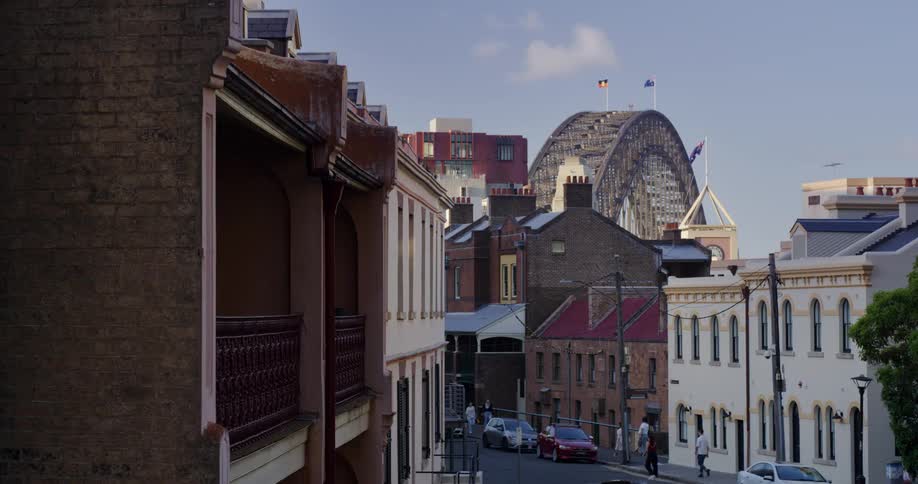 Pedestrians walks along street with arched bridge in the background