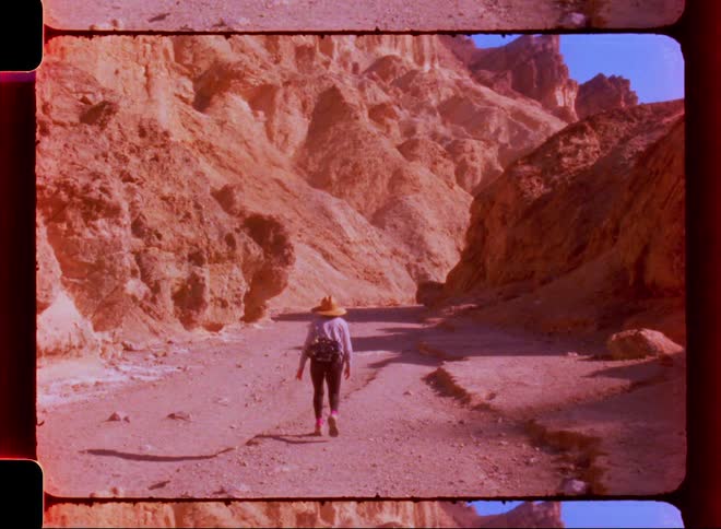 An old video of a person wearing a hat walking on a dirt path between huge rocks
