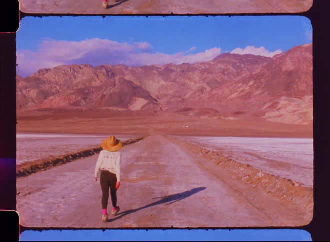 Woman wearing sunhat walks across icy road towardmountains on a cloudy winter day