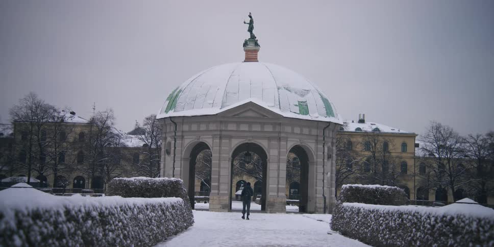A domed structure at the center of a snowy park with a person walking through