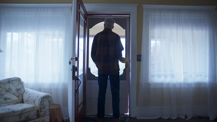 An elderly man stands in a doorway looking outside