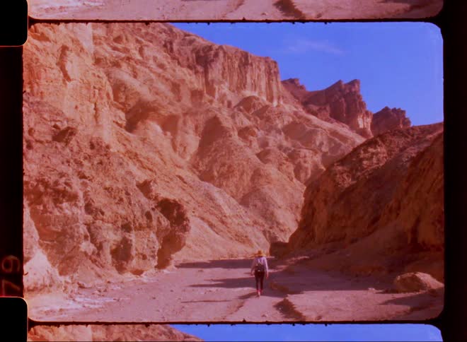 View of a person from behind walking next to rocks and a canyon on a blue sky day