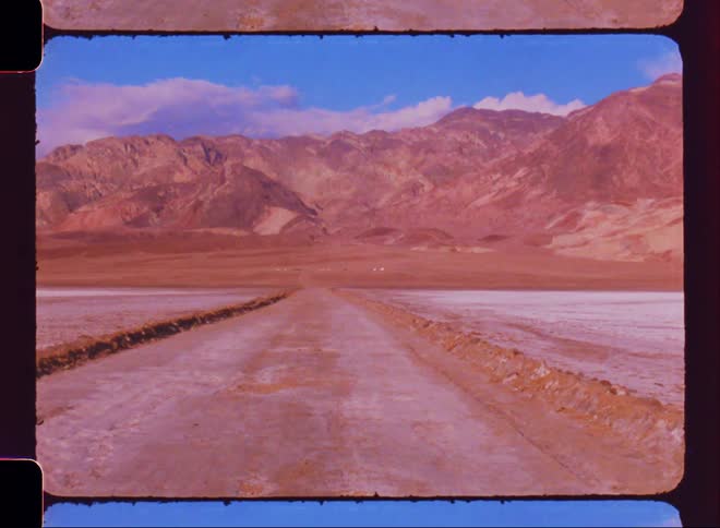 Dirt road in a desert location with mountains on the horizon on a blue sky day with clouds