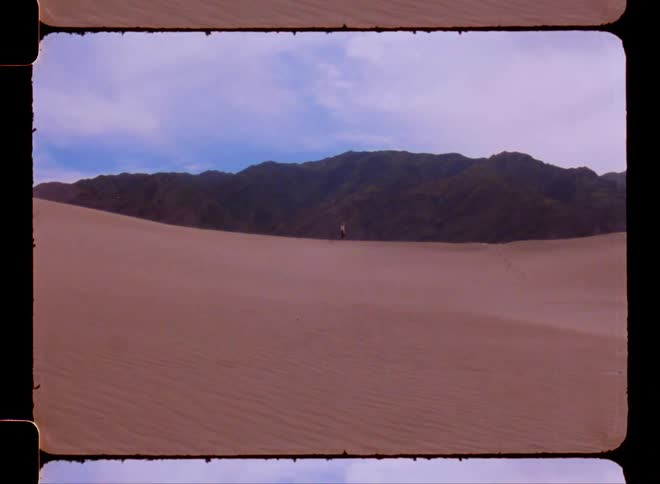 A person walking on the sand dunes on a desert next to the mountains