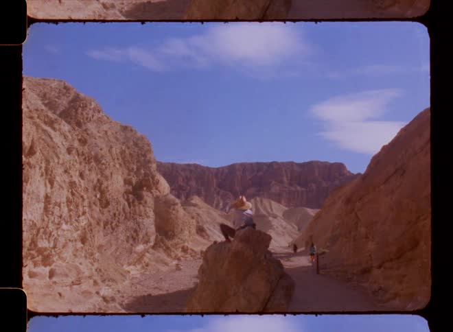 Person sitting on a rock in the middle of a natural environment with canyons and on a blue sky day with few clouds
