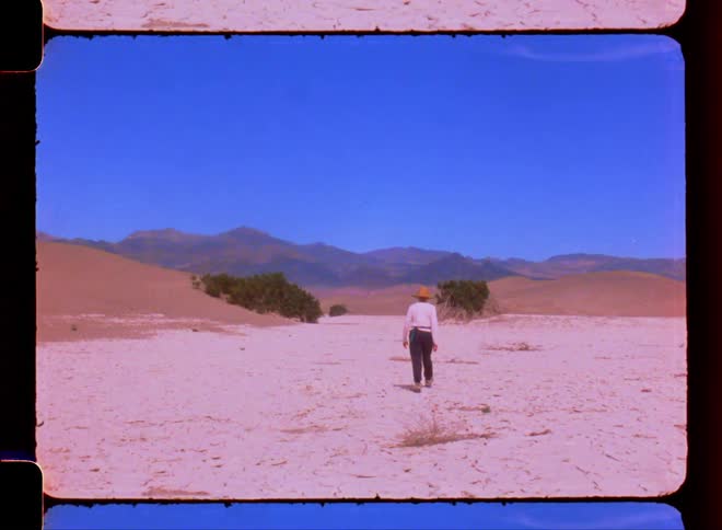 Woman hiking through the desert with mountains on the horizon on a blue sky day