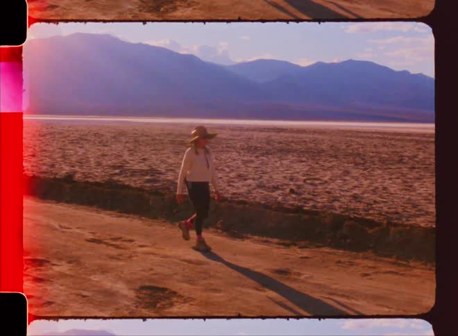 An old video of a person walking on a path in the desert and behind them are large mountains