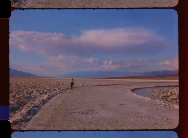 Woman walks across snow covered land bordering icy water on a cloudy day