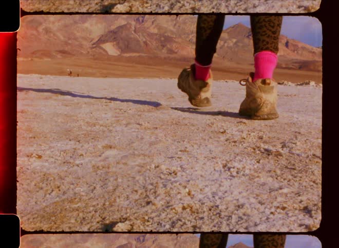 Legs of a woman with boots walking on a desert soil with mountains around on a blue sky day with clouds