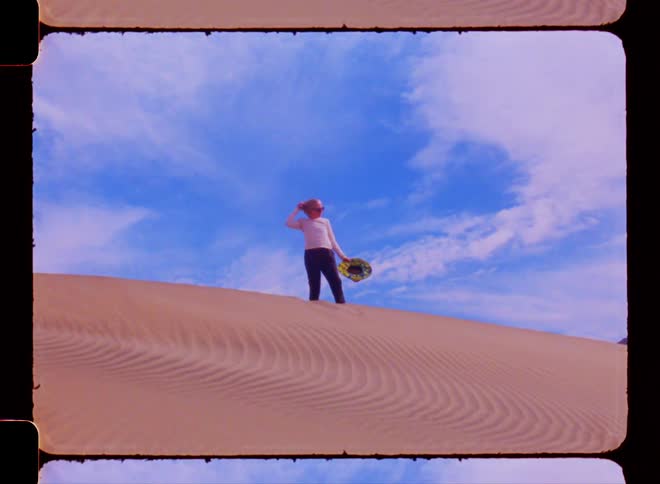 A woman in a desert removes her hat and pulls on her hair
