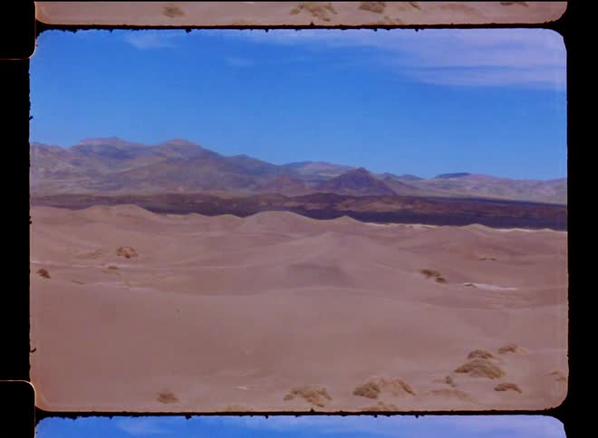 Dune landscape in the desert with mountains on the horizon on a blue sky day