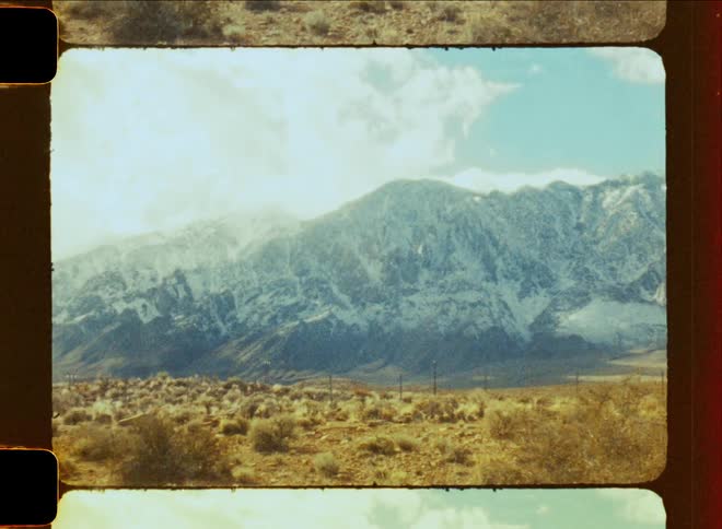 A desert valley sits at the base of a snowcovered mountain range on a partly sunny day