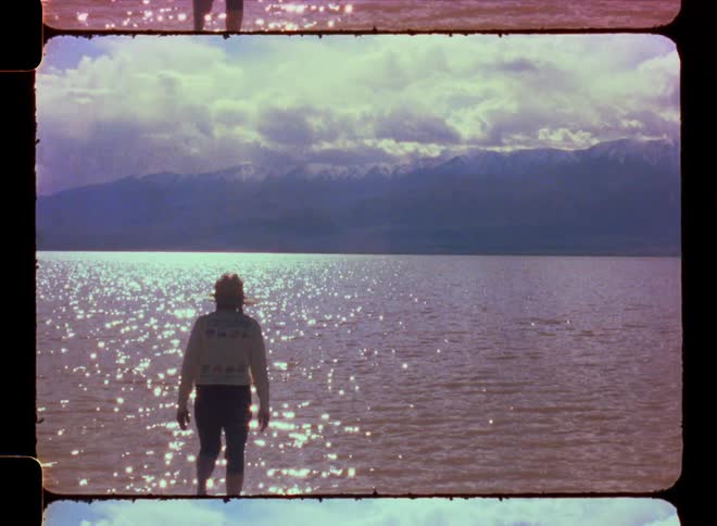 View of a person from behind walking in a shallow sea with mountains on the horizon