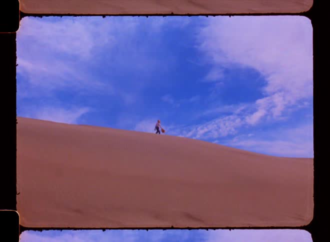 Woman walking on the peak of a desert dune on a blue sky day with clouds
