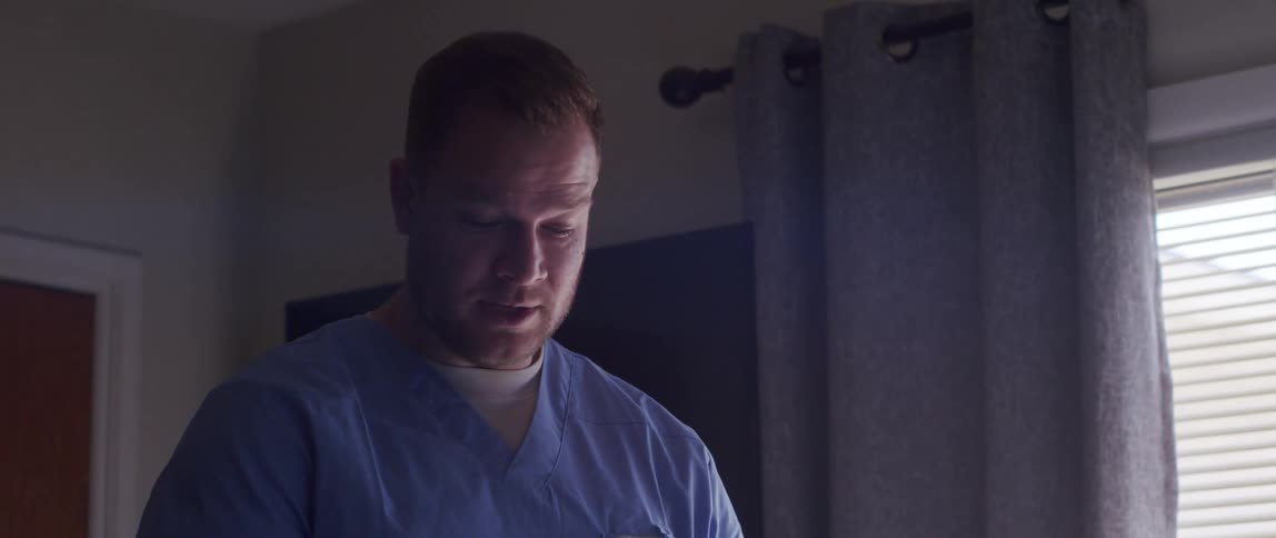 A male nurse enters a room talking to a patient and taking notes
