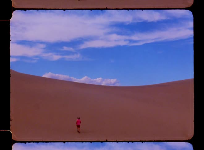 A person in pink walking on sand dunes under a blue sky with clouds
