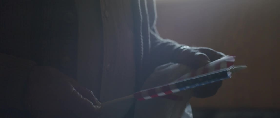 A man stands in a room rolling up a small American flag