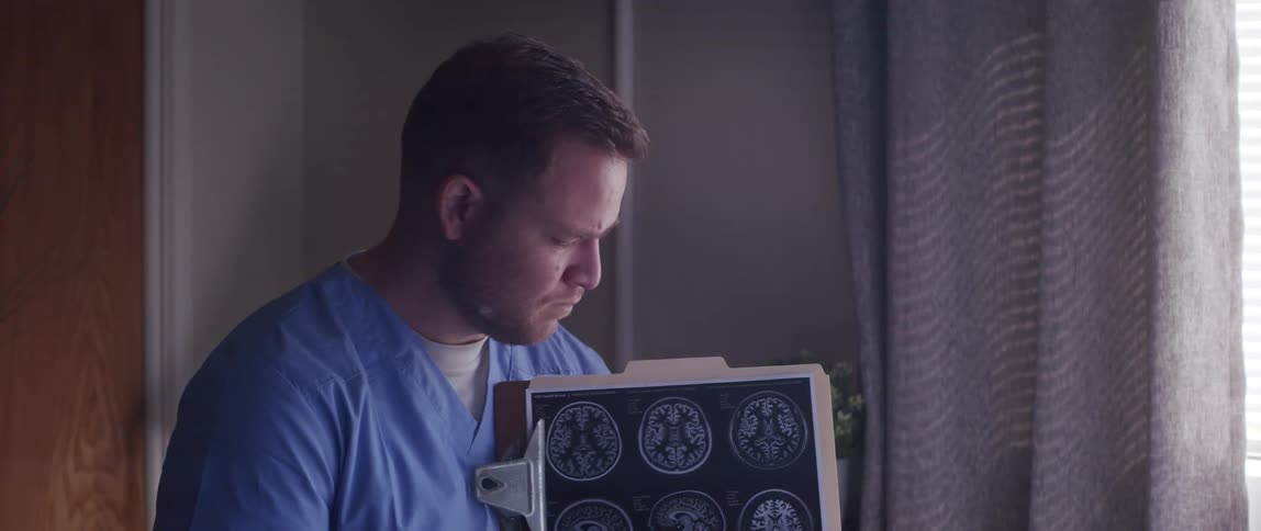 A face of a man who is talking and pointing to a board with some images of brains