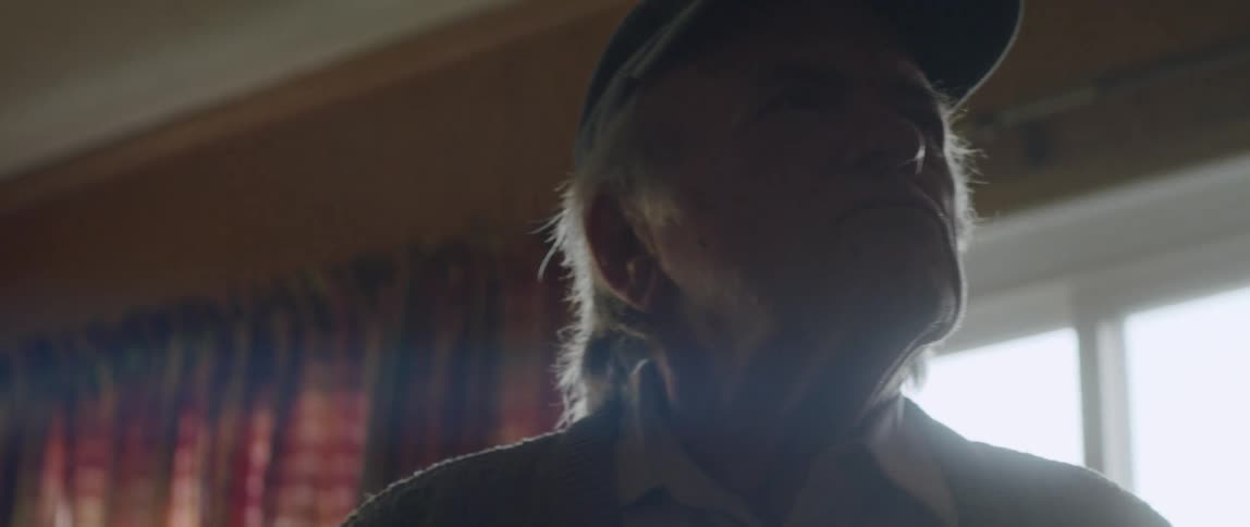 An old man contemplates while walking in a room