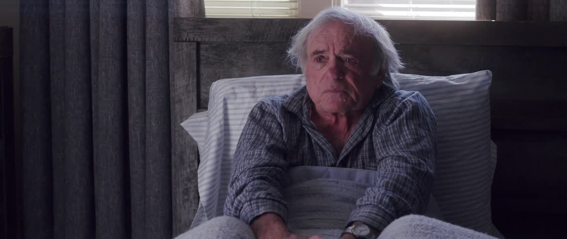 Elderly man resting in bed slumps on the pillows after a conversation