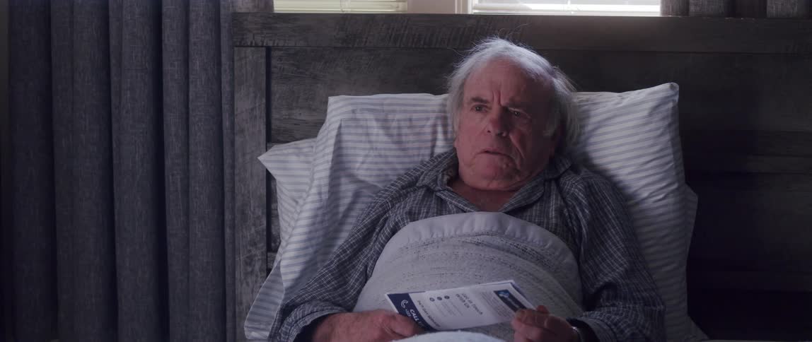 Elderly man resting in bed talks to someone while holding a brochure