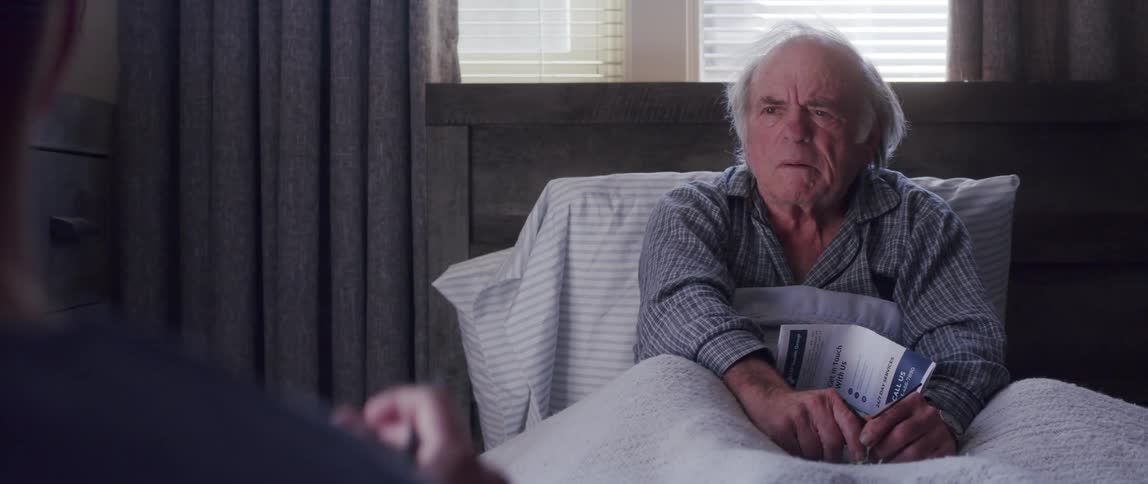 Elderly man lying in bed at home talks to man wearing scrubs